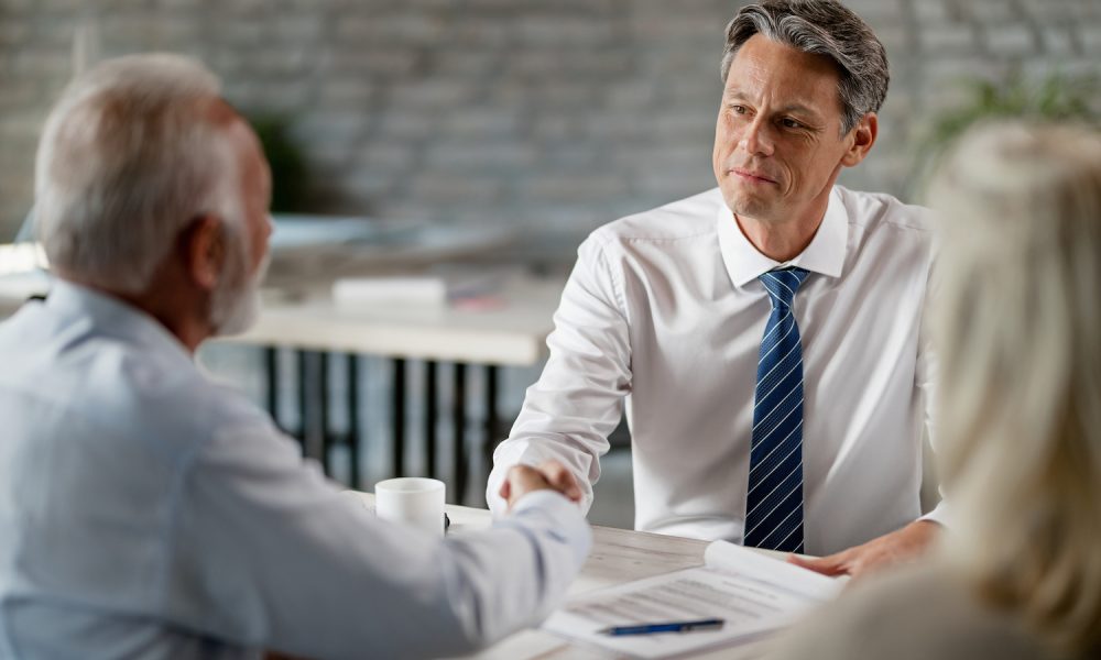 Happy real estate agent and senior clients shaking hands after successful meeting in the office.